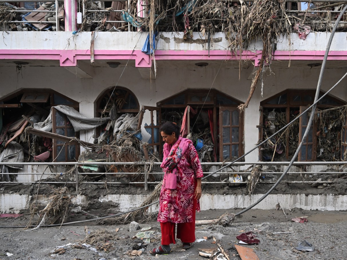 Mulher diante de uma residência atingida no Nepal
